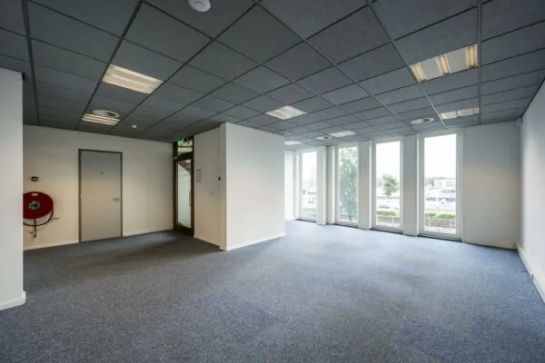 Lege kantoorruimte aan de De Ruijterkade met grote ramen en blauw tapijt.